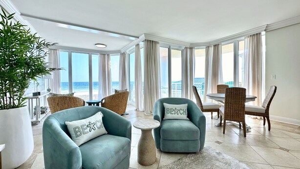 A spacious living room with a view of the ocean, featuring a sofa, armchairs, a small table, and a dining area with wicker chairs.