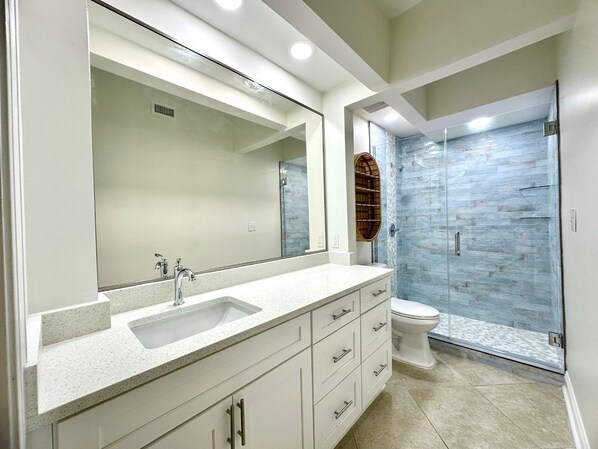 Un baño moderno con un espejo grande, un lavamanos, un inodoro y una cabina de ducha de vidrio.