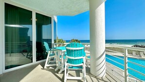 A balcony with a view of the ocean, a pool, and a table with chairs.