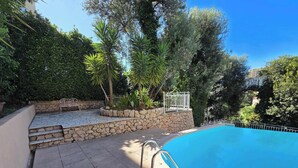 A swimming pool with stone steps leading up to a white metal fence, surrounded by lush greenery and a clear blue sky. - LX146 - Studio cosy avec balcon & vue mer - Monaco (Beausoleil)