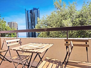 A balcony with a table and chairs, overlooking a cityscape with tall buildings and greenery.
