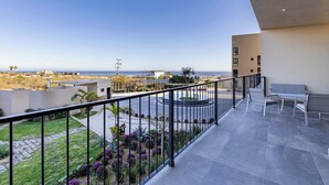 A balcony with a view of the sea, a seating area, and a garden.