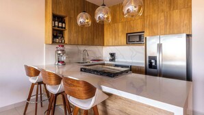 A modern kitchen with wooden cabinets, a stainless steel refrigerator, a built-in microwave, and a central island with bar stools.