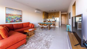 A modern living room with a sofa, a dining table, and a kitchen area in the background.
