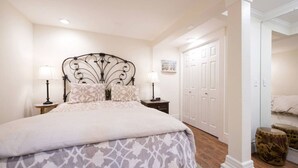 Une chambre à coucher bien rangée, avec un grand lit, des lampes de chevet, une armoire et un petit tabouret.