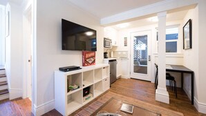 Un espace de vie compact comprenant un téléviseur à écran plat, une bibliothèque, un coin cuisine avec un four à micro-ondes et une table à manger avec des chaises.