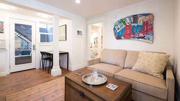 Un salon comprenant un canapé, une table basse, un coin repas avec une table et des chaises, et un tableau coloré accroché au mur.