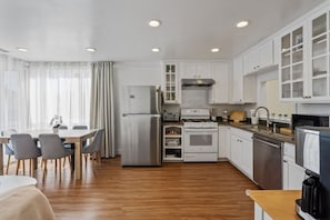 A modern kitchen with white cabinets, stainless steel appliances, and a wooden dining table with chairs. - Sunset Haven: Corner House with lots of Light (San Francisco)
