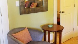 A room with a grey armchair, a small round wooden table, and a mirror on the wall. - Roomy Studio Walkable to UC Berkeley w/parking (Berkeley)