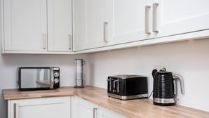 Una cocina con armarios blancos, microondas, tostadora y cafetera sobre una encimera de madera.