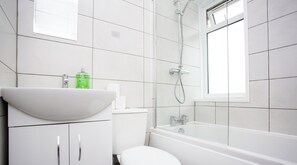 Une salle de bain avec un lavabo, des toilettes et une baignoire blancs, et une fenêtre située au-dessus de la baignoire.