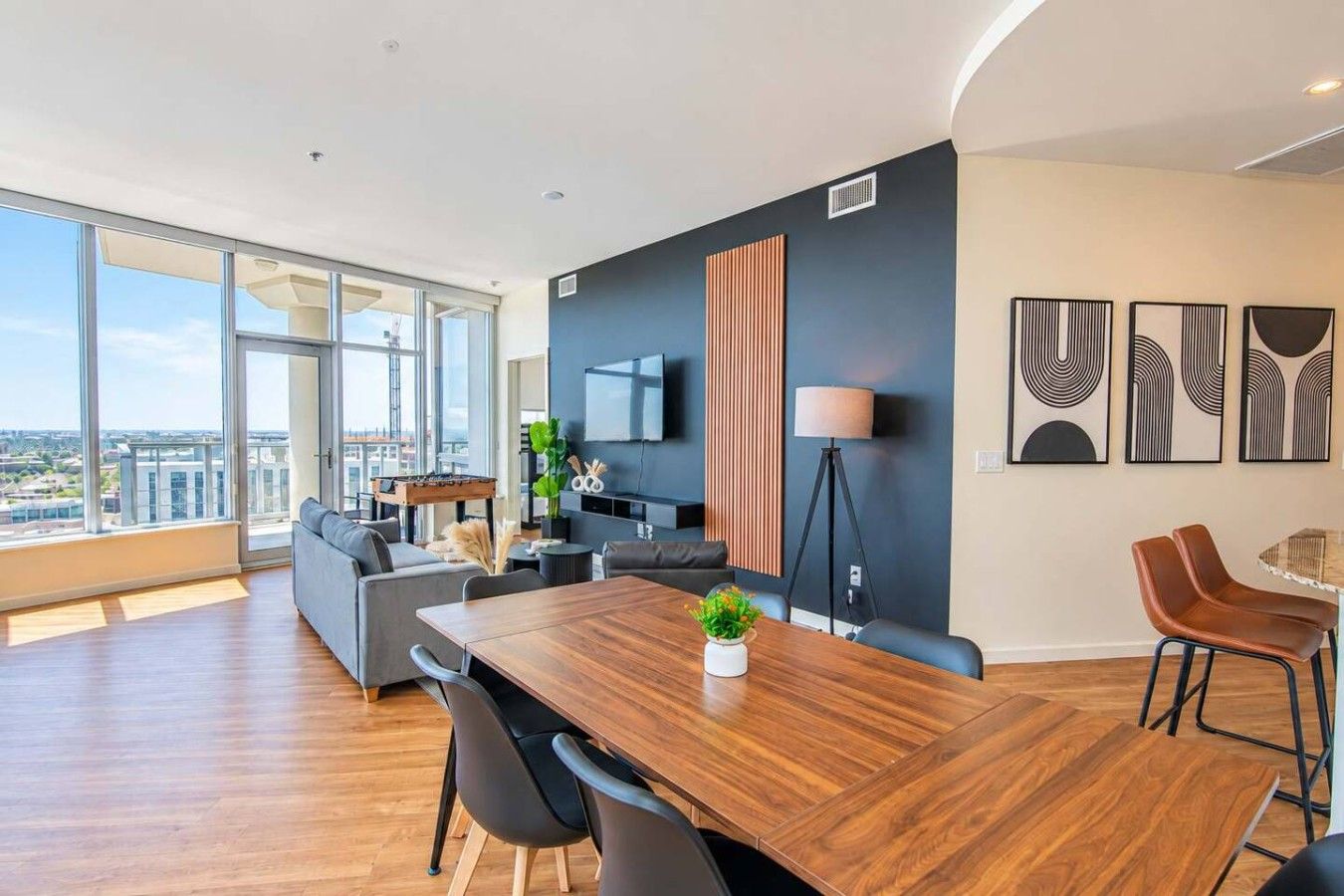 A modern living room with a large window, a wooden dining table, and a sofa.