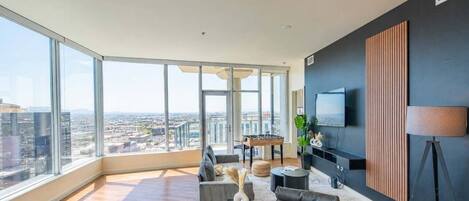A spacious living room with a large window, a flat-screen TV mounted on the wall, and a foamy white sofa.