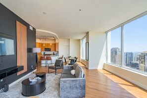 A modern living room with a flat-screen TV, a sofa, a coffee table, and a dining area with chairs.