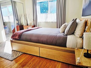 Een moderne slaapkamer met een houten bed, een nachtkastje met lamp en uitzicht op de omgeving door het raam.