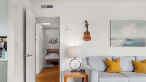 A modern living room with a grey sofa, a wooden side table, a lamp, a guitar, and a painting on the wall. - Seabright Breeze (Santa Cruz)