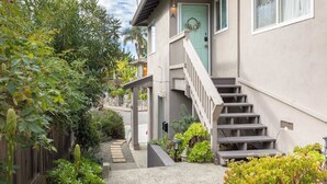 A residential building with a light green door, a wooden staircase, and a small garden area with various plants. - Seabright Breeze (Santa Cruz)