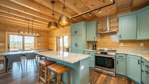 A modern kitchen with a large island, stainless steel appliances, and light blue cabinets. - Spacious Lodge w/ Hot Tub, Fire Pit & Games (Swanton)