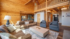 A spacious living area with a high ceiling, wooden walls, and a balcony. - Spacious Lodge w/ Hot Tub, Fire Pit & Games (Swanton)