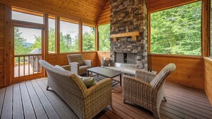 A wooden deck with wicker furniture and a stone fireplace. - Spacious Lodge w/ Hot Tub, Fire Pit & Games (Swanton)
