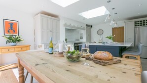 A modern kitchen with a wooden dining table, a built-in island, and a large window above the sink. - One Beach Road - sleeps 10 guests  in 5 bedrooms (Rhosneigr)