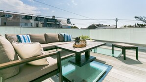 A rooftop terrace with a glass-enclosed pool, a wooden table with bottles and glasses, and a sofa with cushions. - One Beach Road - sleeps 10 guests  in 5 bedrooms (Rhosneigr)