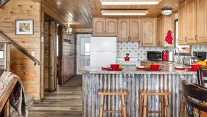 Eine rustikale Küche mit Holzschränken, einer zentralen Kochinsel mit Barhocker und einem Kühlschrank.