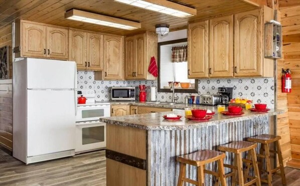 Una cucina con mobili in legno, un frigorifero bianco, un forno a microonde, un fornello e un piano di lavoro in granito con sgabelli.