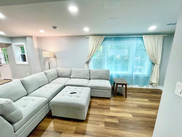 A modern living room with a sectional sofa, a small table, and a large window with curtains.