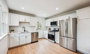 A modern kitchen with white cabinetry, stainless steel appliances, and a wooden floor.