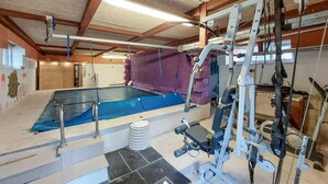 En swimmingpool med en hoppställning, omgiven av träningsredskap och en lila, vadderad vägg.