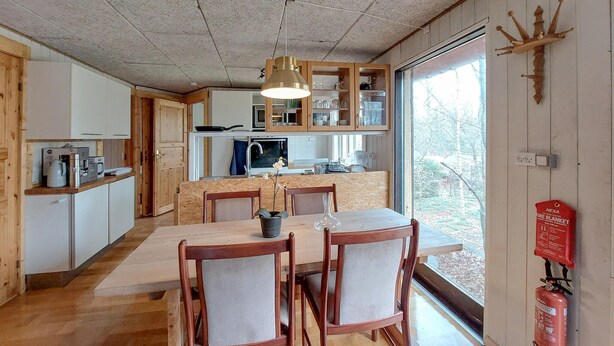 A cozy kitchen with wooden cabinets, a dining table with chairs, and a large window offering a view of trees. - Cozy apartment in åsljunga with sauna (Åsljunga)