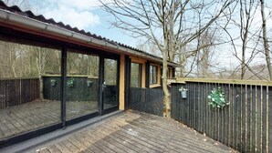 A wooden deck with a glass enclosure, a wooden fence, and a tree. - Cozy apartment in åsljunga with sauna (Åsljunga)
