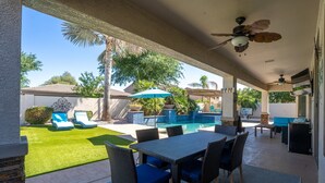 A covered outdoor area with a pool, lounge chairs, and a table with chairs.