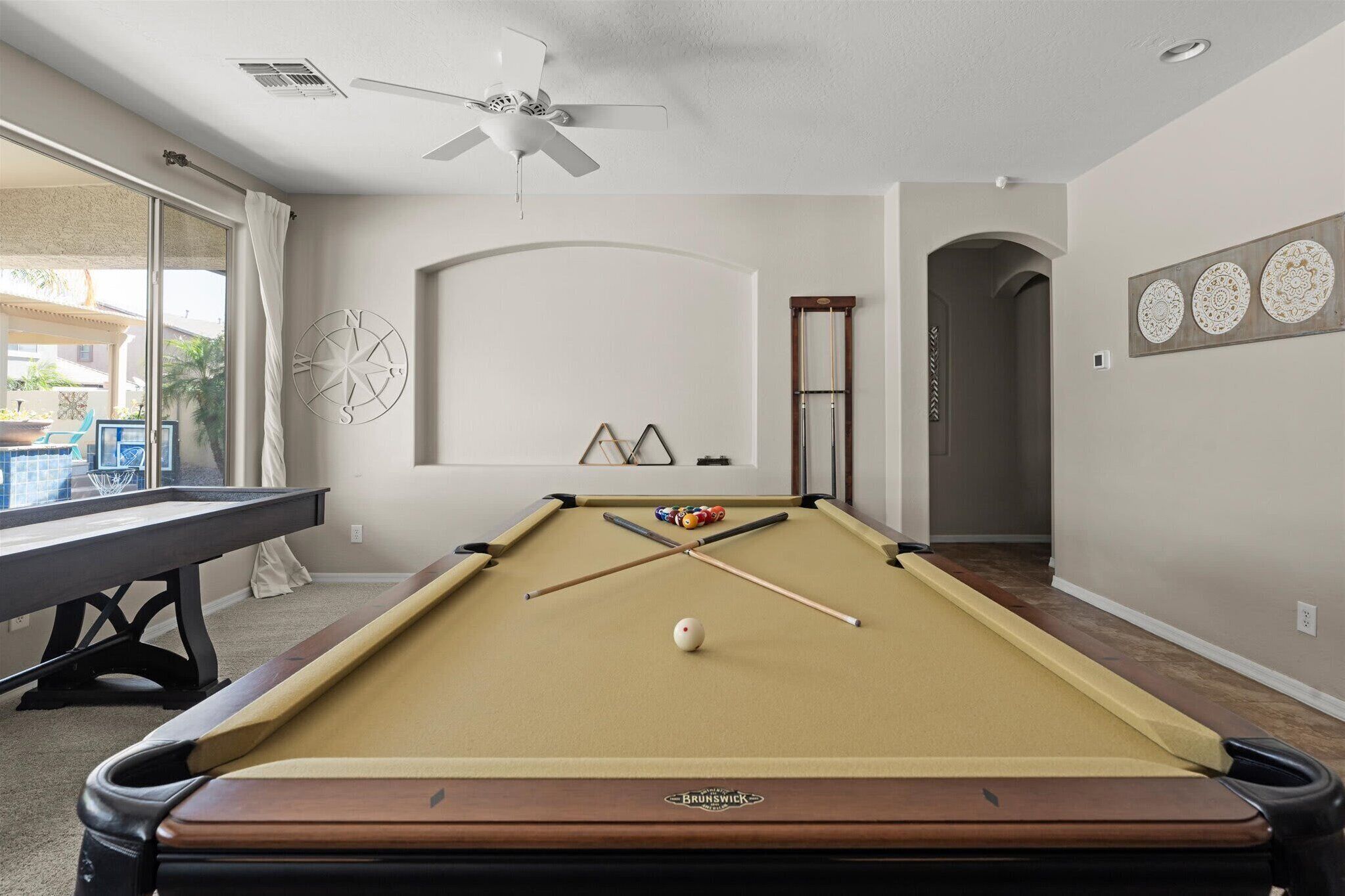 A pool table with a compass wall decoration, a ceiling fan, and a view of the outdoors.