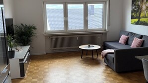 A modern living room with a grey sofa, a small round table, and a potted plant. - Vacation apartment Klaus (Clausen)