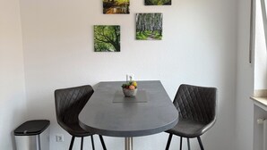 A modern dining area with a round table, two chairs, and a trash bin. There are four framed pictures on the wall. - Vacation apartment Klaus (Clausen)