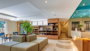 A modern hotel lobby with a seating area, a reception desk, and a large bookshelf.