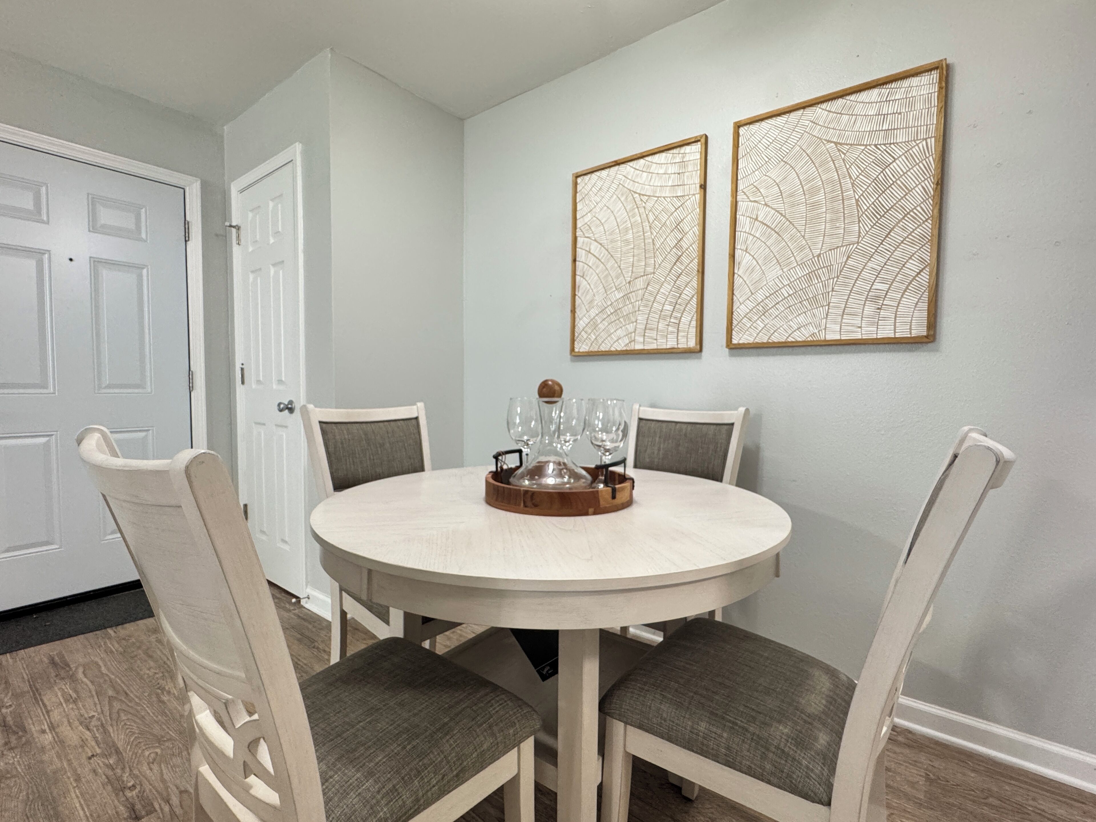 A round dining table with four chairs, a tray with glasses, and two framed wall art pieces.