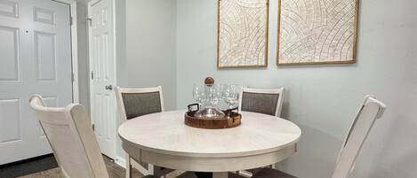 A round dining table with four chairs, a tray with glasses, and two framed wall art pieces.