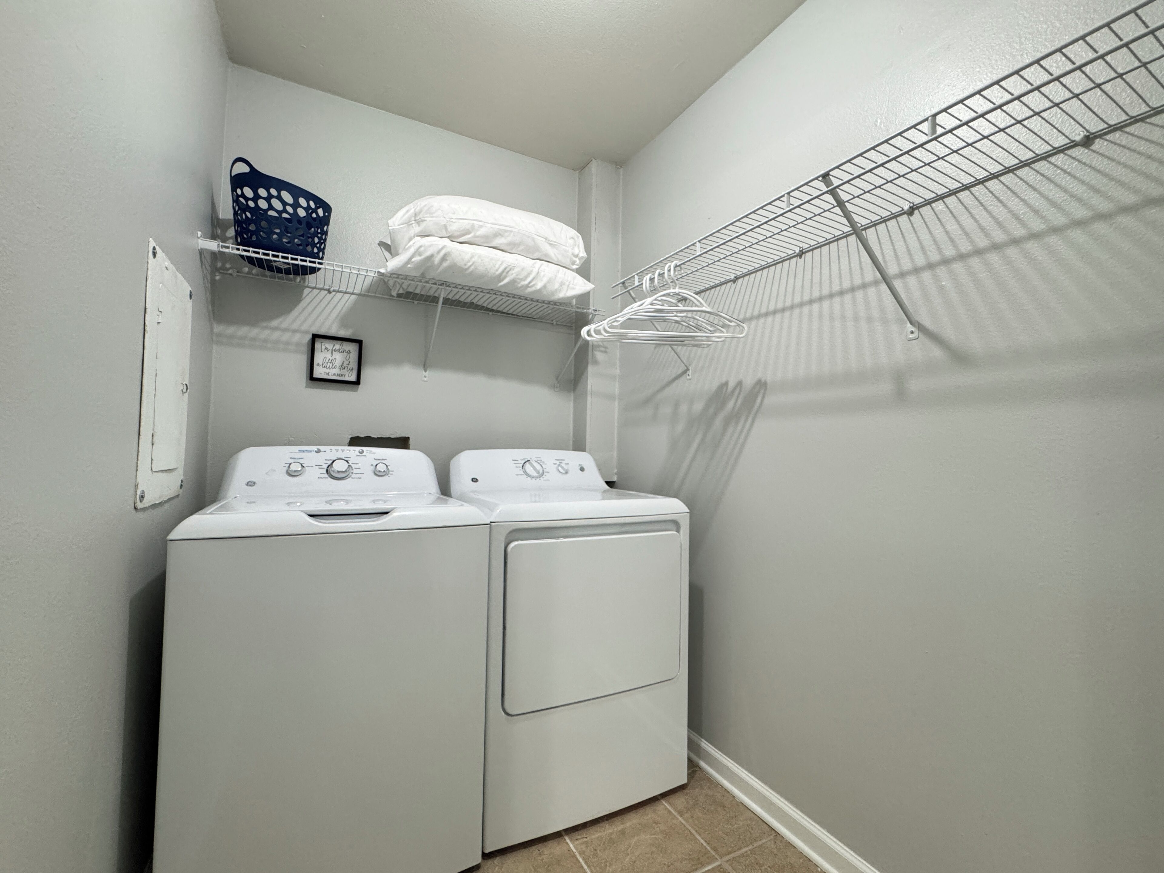 A laundry room with two stacked washers and dryers, a drying rack, and a shelf with folded towels.