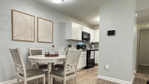 Een moderne keuken met witte kasten, een zwarte magnetron en een eethoek met een ronde tafel en stoelen.