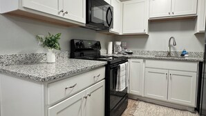 Een moderne keuken met witte kastjes, een zwarte magnetron, een fornuis en een granieten aanrecht.