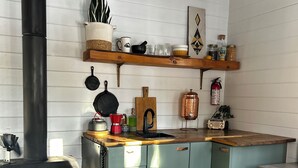 Una cocina con estufa de leña, un lavabo, armarios y diversos utensilios de cocina.