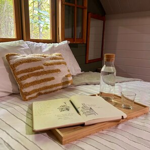 Ein Schlafzimmer mit Bett, Fenster, Kissen, einem Buch, einem Stift, einem Glas und einer Flasche.