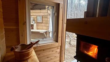 A wooden cabin interior with a fireplace, a window, and a wooden bench.