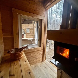 Ein Holzblockhaus-Interieur mit Kamin, Fenster und einer hölzernen Bank.