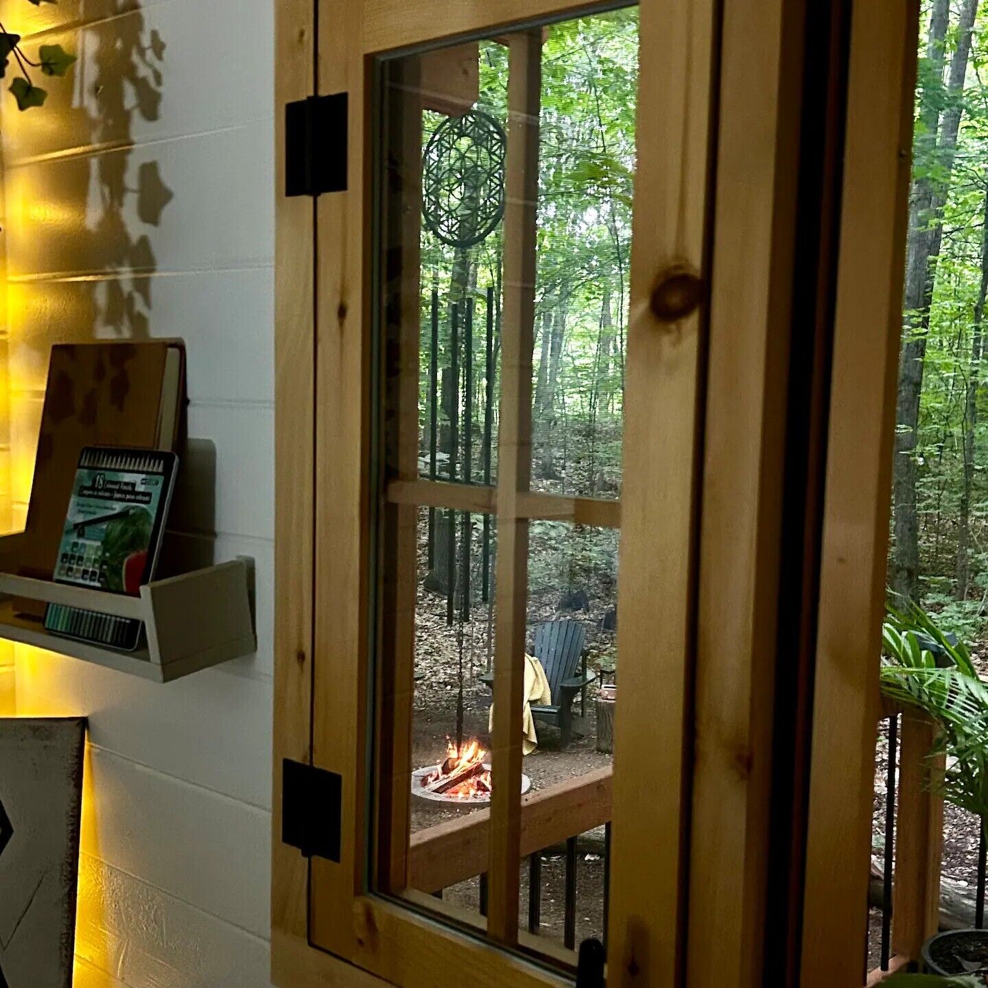 A wooden-framed window with a view of an outdoor fire pit area, surrounded by trees.