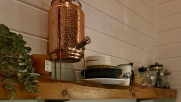Una cocina con estantes de madera, una olla de cobre, un fregadero y una planta.