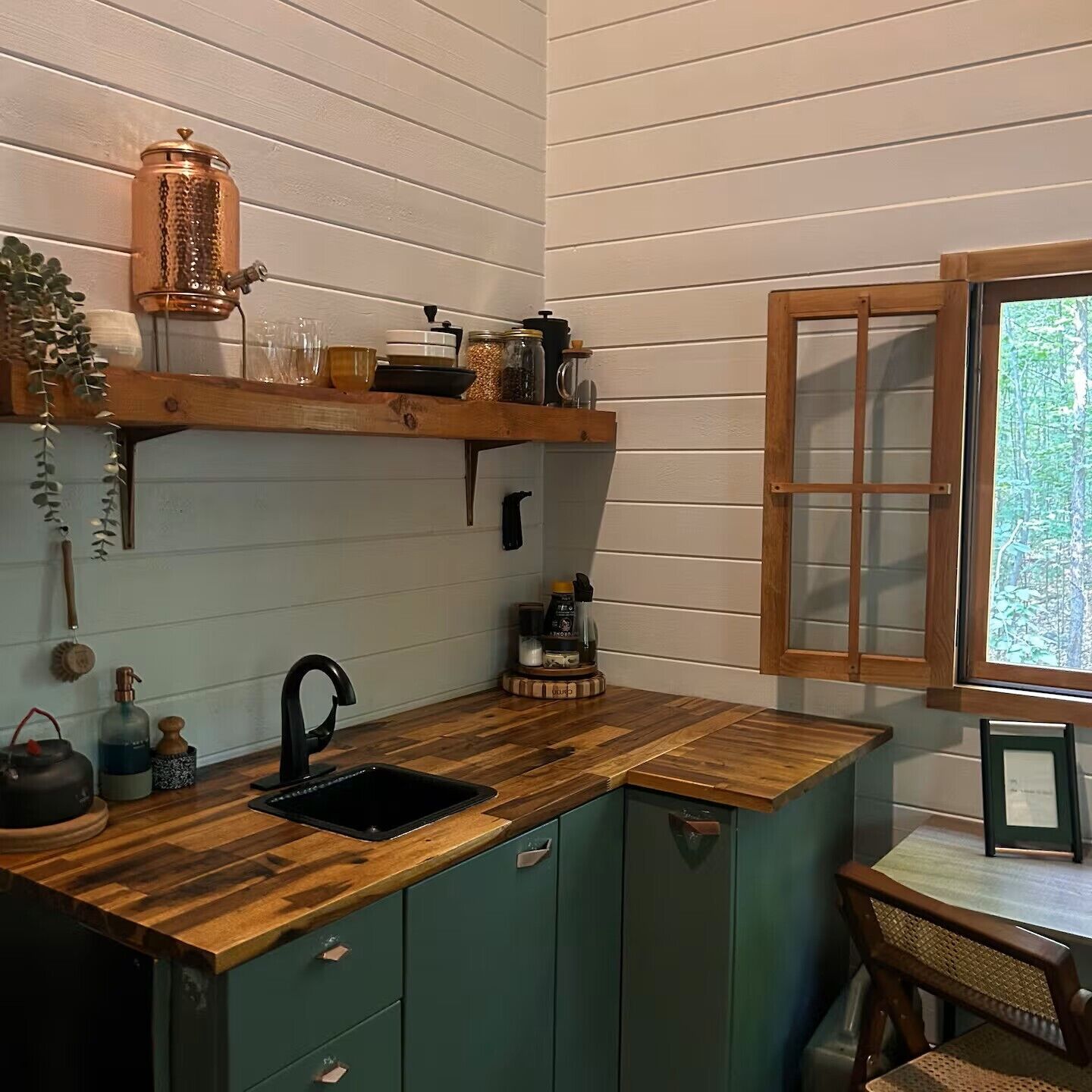 Une cuisine compacte dotée d’un plan de travail en bois, d’un évier et d’une fenêtre donnant sur un espace verdoyant.